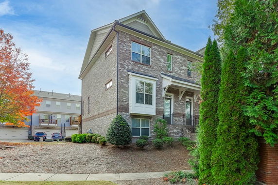 Side view of a multi-story brick house with a small porch and windows.