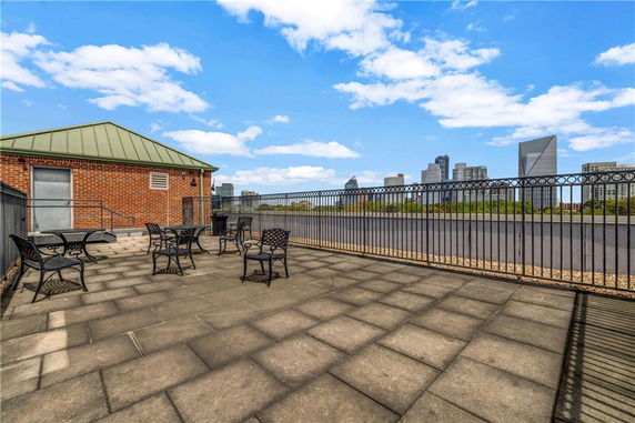 Rooftop area with seating and metal fencing, overlooking cityscape.