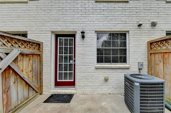 Rear view of a house with a glass-panel door, window, and air conditioning unit on the exterior brick wall.
