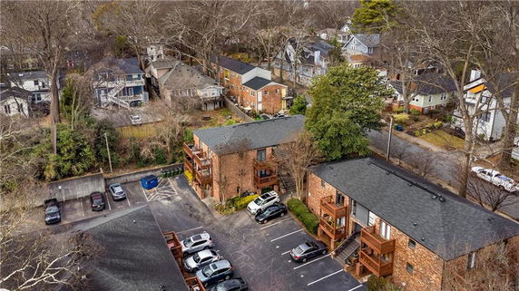 Aerial view of residential buildings surrounded by trees and a parking area.