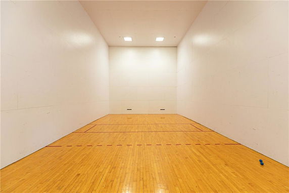 Interior view of an indoor racquetball or squash court with wooden flooring and white walls.