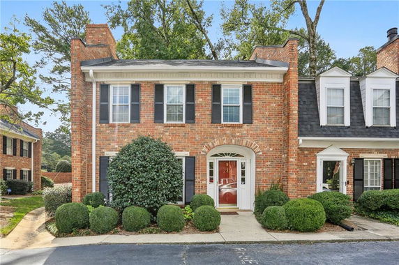 Front view of a two-story brick townhouse with a red door and black shutters.