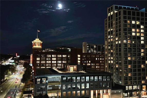 Night view of multiple buildings and streets in an urban area under a full moon.