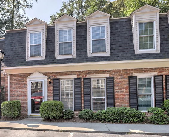 Front view of a brick house with dormer windows and black shutters.