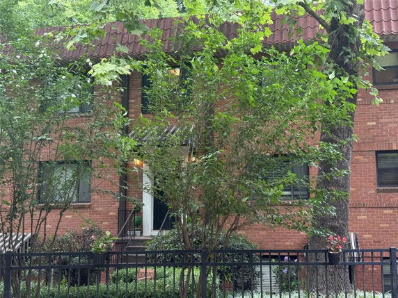 Front view of a brick apartment building with a sloped roof and a metal fence.