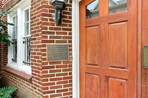 Close-up view of a brick building entrance with a wooden door and a plaque.