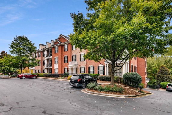 Front view of a red brick multi-story building with white trim and a parking area in front.