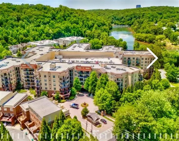 Aerial view of a large residential building complex surrounded by trees and a nearby body of water.