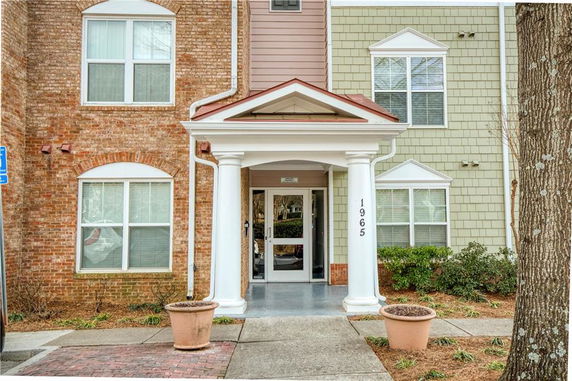 Front view of a multi-story building with a brick and siding exterior, featuring a covered entrance with columns.