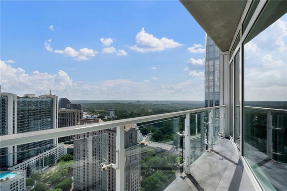 Panoramic view from a high-rise building balcony with glass railing overlooking the cityscape.