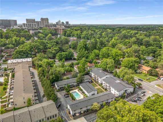 Aerial view of residential buildings surrounded by trees and greenery, with a city skyline in the background.