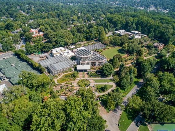 Aerial panoramic view of a large building complex surrounded by lush greenery and pathways.