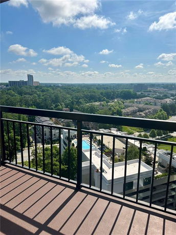 View from a high-rise balcony overlooking a cityscape with buildings, trees, and a distant skyline.