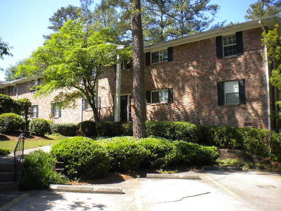 Front view of a brick, two-story building with windows and surrounding greenery.