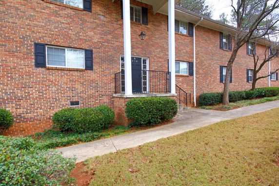 Front view of a two-story brick building with black shutters and a small porch with white columns.