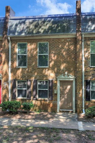 Front view of a two-story brick townhouse with double windows and a brown door.