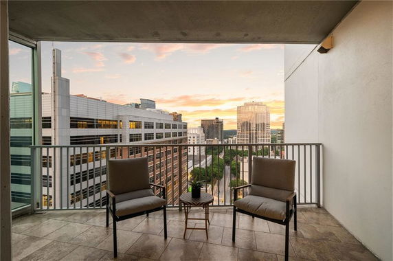 Balcony view overlooking a cityscape with multiple buildings and a sunset in the background.