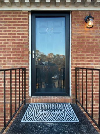 Entrance of a brick house with a black door and a welcome mat.