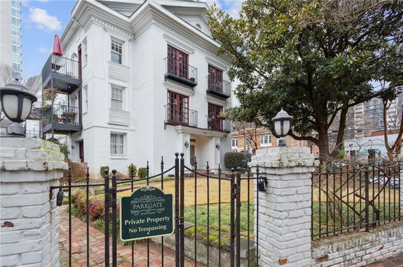 Front view of a white multi-story building with balconies and a gated entrance.