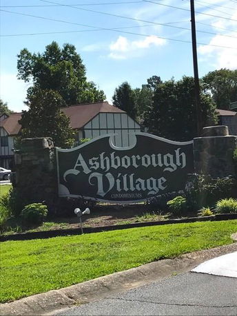 Front view of Ashborough Village Condominiums signage with condominium buildings in the background.