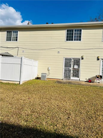 Rear view of a two-story house with light yellow siding and fenced patio area.