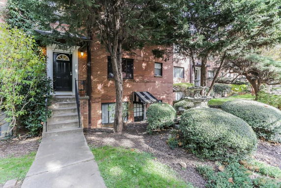 Front view of a multi-story brick house with trees and shrubs.