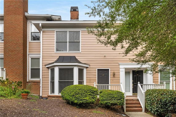 Front view of a two-story townhouse with a central bay window and a brick chimney.