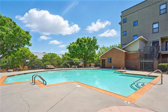Outdoor swimming pool next to a building with surrounding greenery.