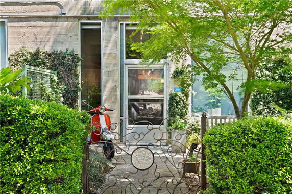 Front view of a building entrance with a glass door and large windows, surrounded by greenery and a scooter parked outside.