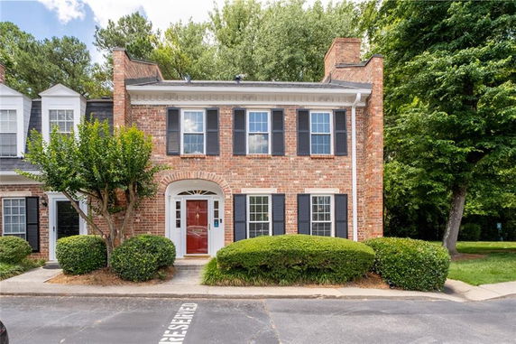 Front view of a two-story brick townhouse with a red door and black shutters.