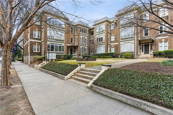 Front view of a multi-story brick apartment building with large windows and stairway entrance.