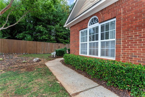 Side view of a brick house with a rectangular window and a hedge along the walkway.
