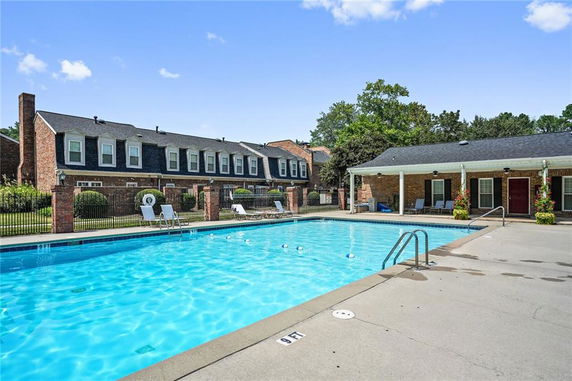 Outdoor swimming pool with adjacent brick buildings and lounging chairs.