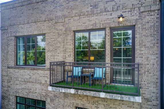 View of a brick building with a small balcony featuring metal railing and two chairs.