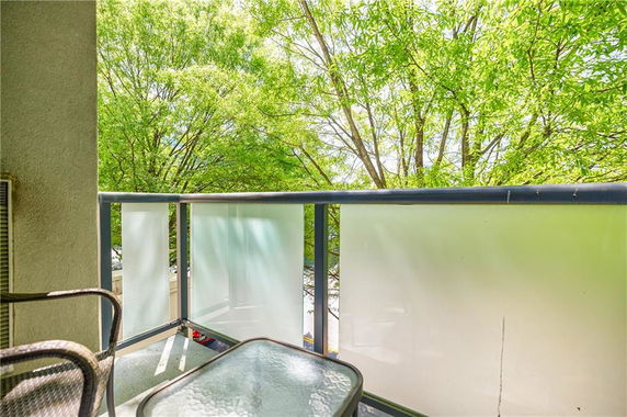 View from a balcony with frosted glass railing, surrounded by leafy trees.