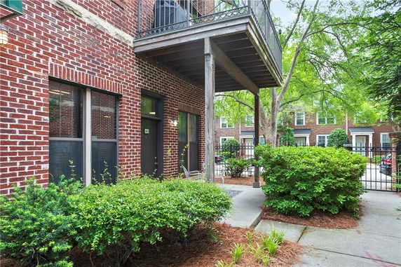 Front view of a brick building with a small balcony and an entrance surrounded by shrubs.