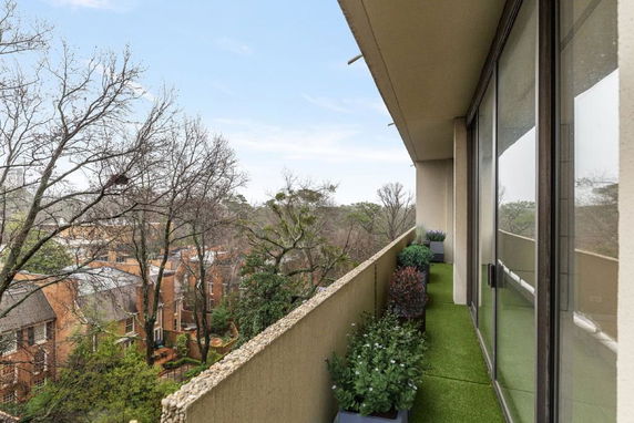 View from a balcony with glass doors overlooking surrounding trees and buildings.