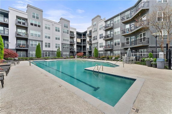 Outdoor swimming pool area surrounded by a multi-story apartment building.