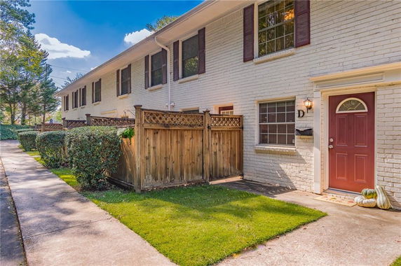 Front view of a two-story townhouse with a fenced patio and red door.