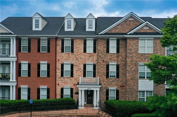 Front view of a multi-story brick building with black shutters and dormer windows.