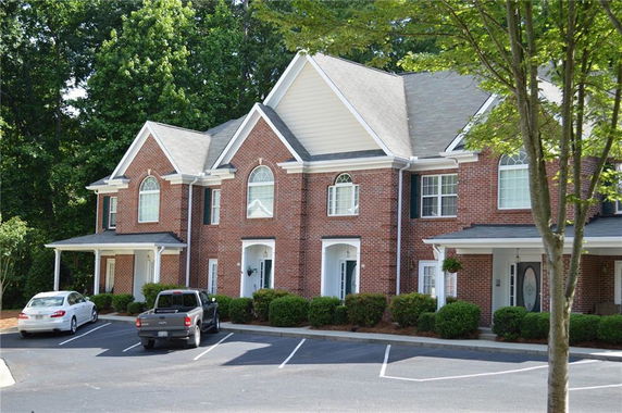 Front view of a two-story brick townhouse with multiple peaked roofs and arched windows.