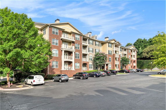 Front view of a multi-story brick apartment building with balconies and parked cars.