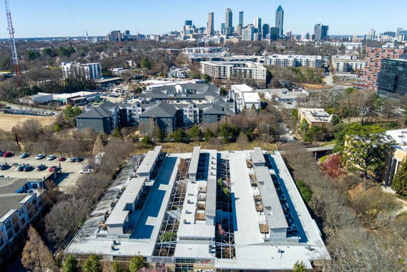 Aerial view of a residential and urban area with buildings, roads, and a city skyline in the background.