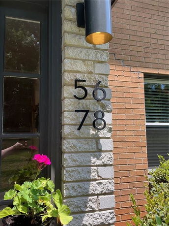 Section of a brick house with house numbers displayed beside the door.