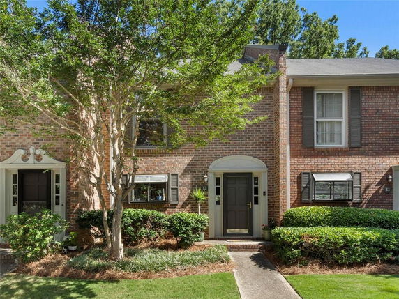 Front view of a two-story brick townhouse with a central entrance and surrounding greenery.