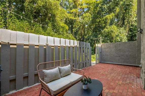 Outdoor patio area with brick flooring, fenced with wooden panels and surrounded by trees.