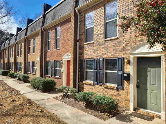 Front view of a row of two-story brick townhouses with green doors and window shutters.