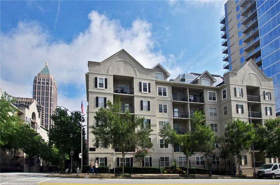 Front view of a multi-story apartment building with balconies and trees in front.