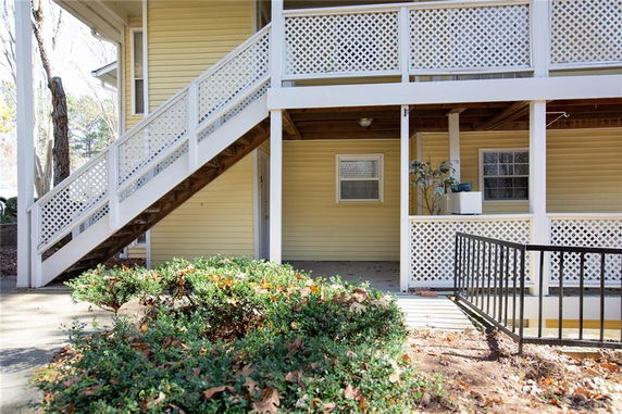 Exterior view of a yellow house with a staircase and balcony with lattice railing.