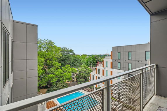 View from a building balcony overlooking a swimming pool and adjacent modern buildings.